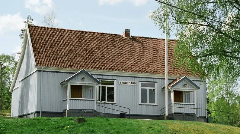 liten gråmålad byggnad med texten bygdegård på fasaden