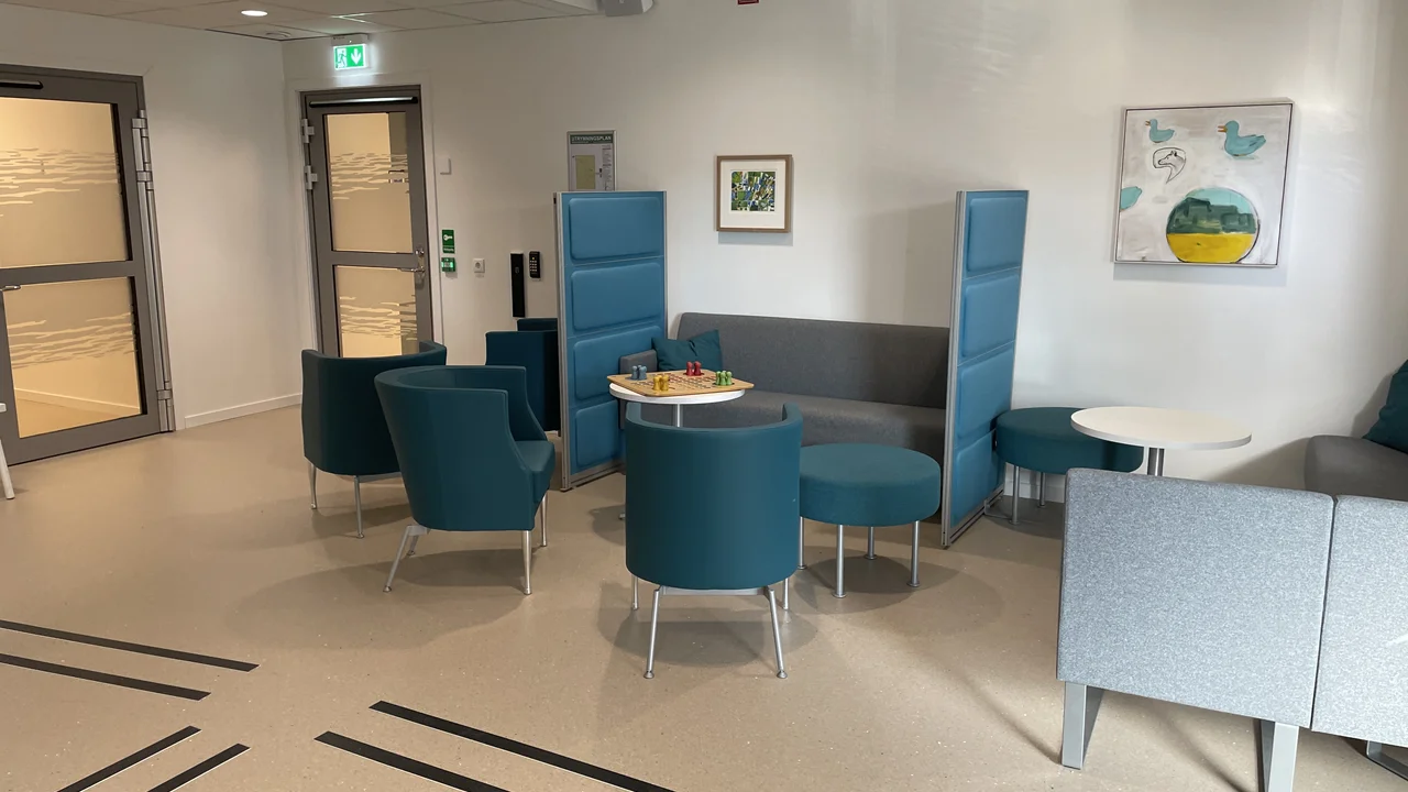 Väntrum med blåa och gråa fåtöljer, samt små vita bord.
