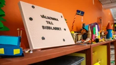 En skylt står längst upp på en hylla. På den står Välkomna till Bibblabbet med stora bokstäver. På den bruna hyllan finns olika skapelser i papper.