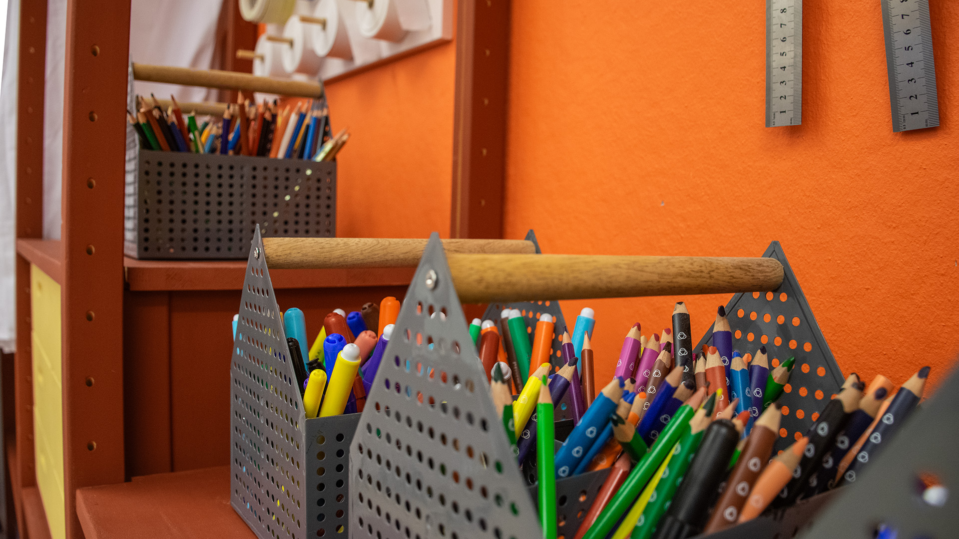 Metalltråg fulla med färgpennor. Metall-linjaler hänger på väggen ovanför dem.