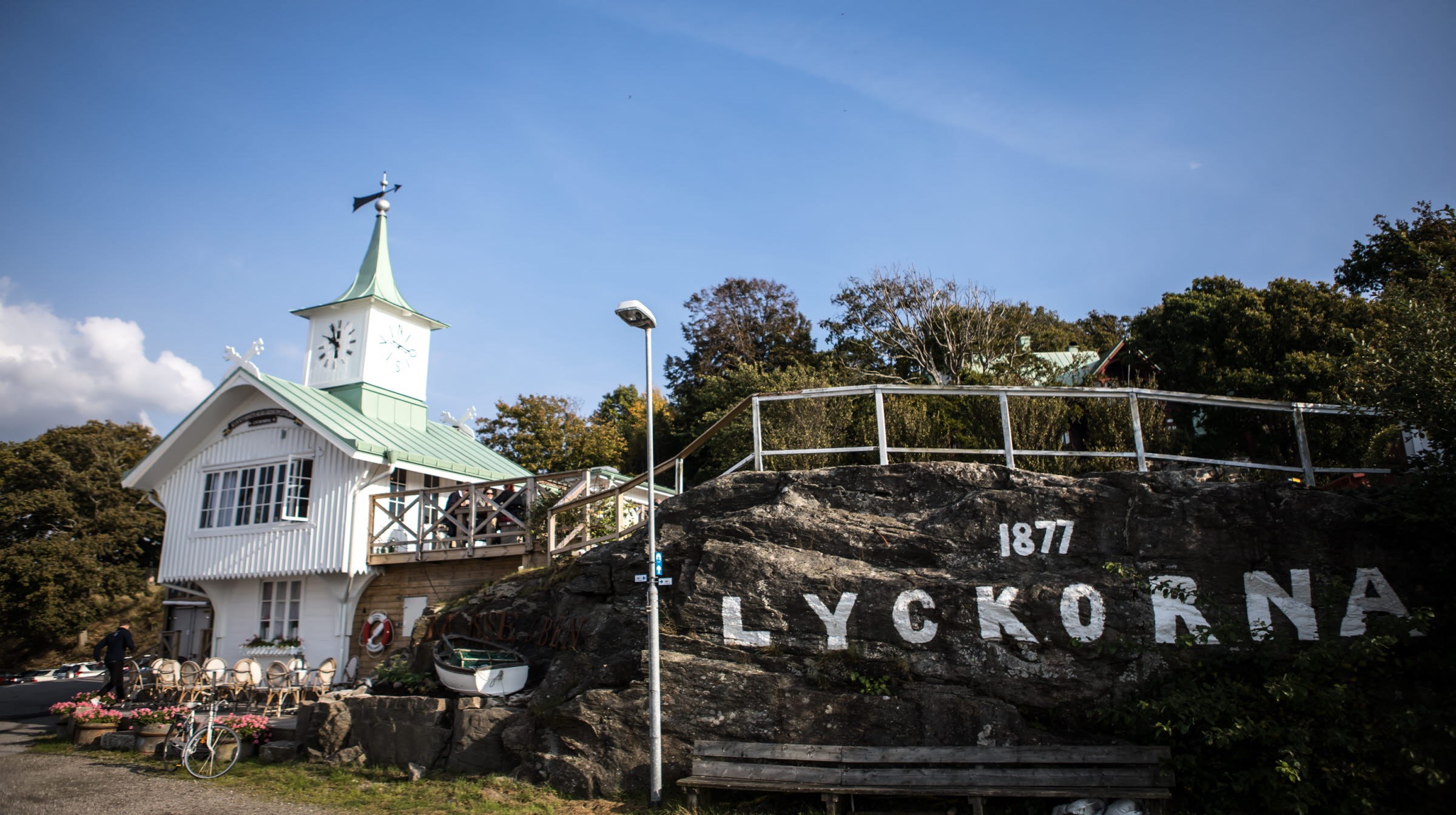 Ett vitt sekelskiftshus med ett klocktorn bredvid en veranda som är byggd på en klippa.