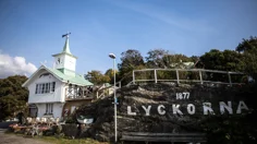 Ett vitt sekelskiftshus med ett klocktorn bredvid en veranda som är byggd på en klippa.