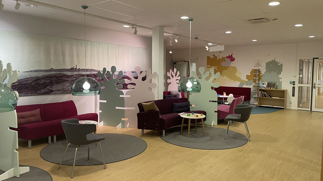 Vöntrum med träfärgat golv, röda och grå sittgrupper.