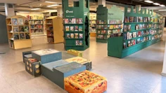 Barnavdelningen LÄS, interiör. Bokhyllor i grönt och ljust trä, böckerna är i många fall placerade med framsidan utåt. En sittmöbel finns mitt i rummet, stora sittytor i olika nivåer. Golvet har en beige plastmatta.