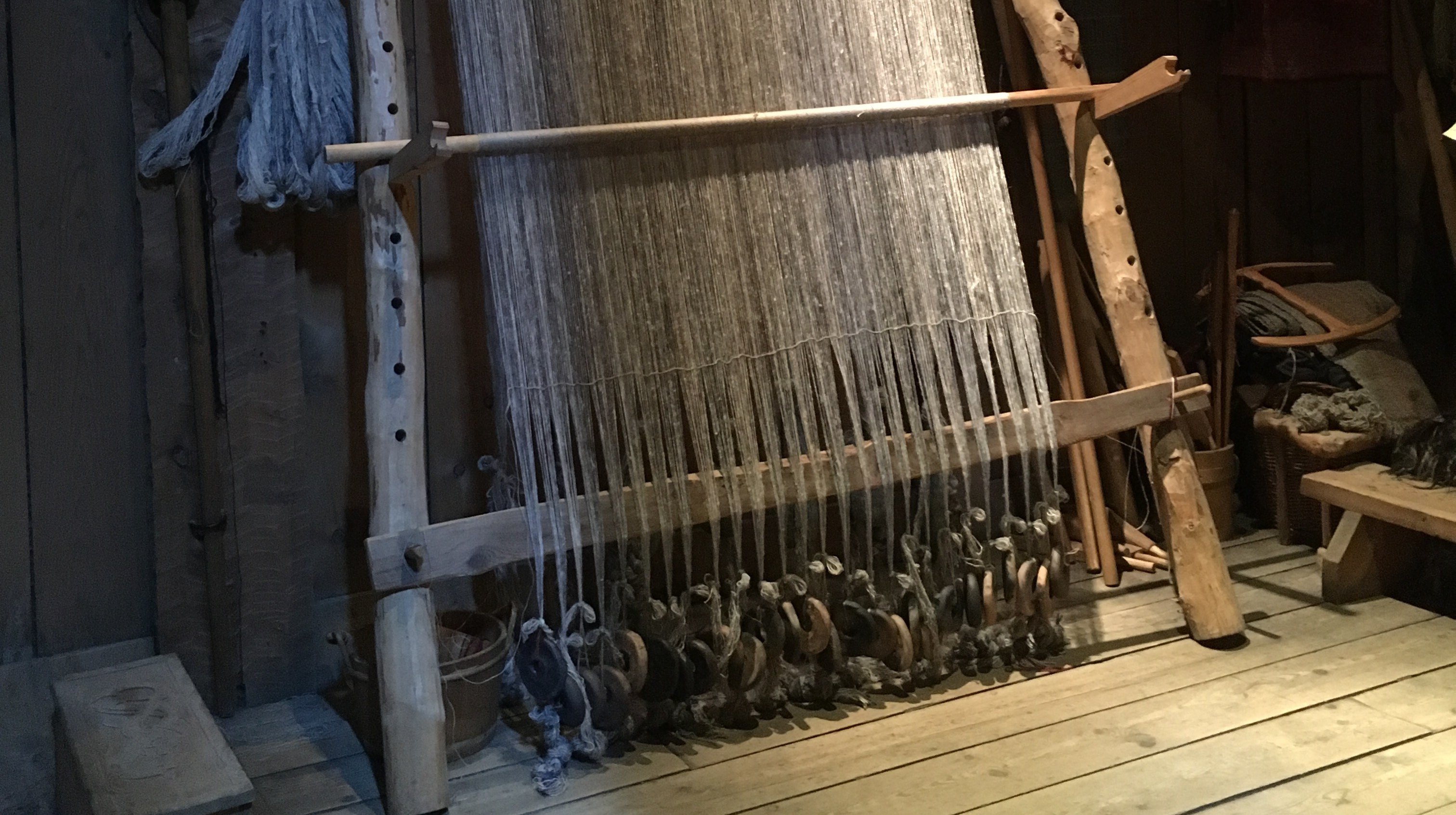 En äldre vävstol med tyngder längst ner på hängande garn
